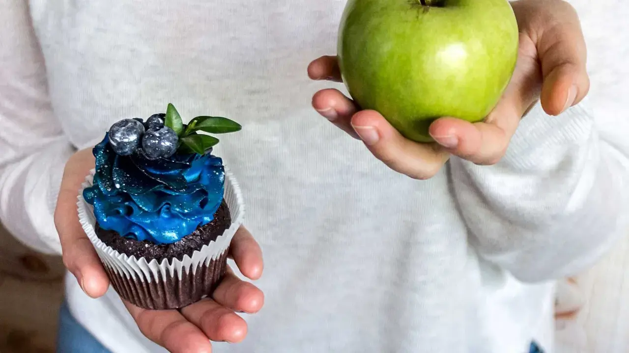 En hand håller ett grönt äpple, den andra en dekorerad cupcake. Ett val för en socker detox.