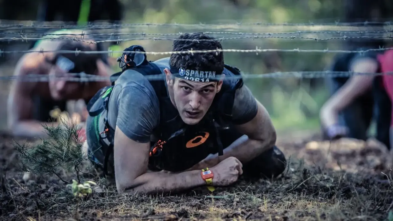 En deltagare i ett ocr sport-lopp kryper under taggtråd.