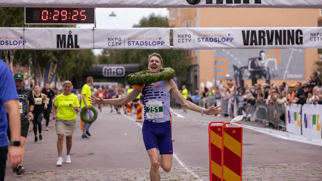 Glad löpare med krans korsar mållinjen i Norrköping stadslopp.