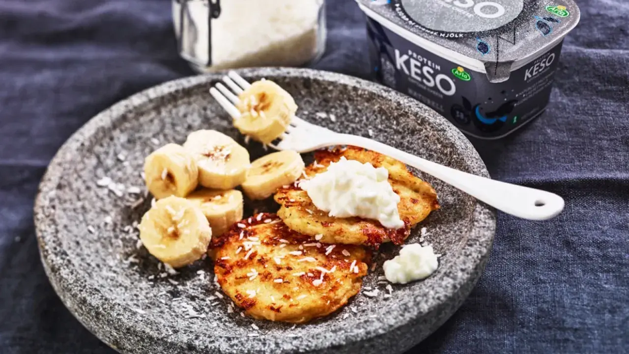 En tallrik med pannkakor toppade med keso och bananskivor. Perfekt för ett proteinrikt keso mellanmål.