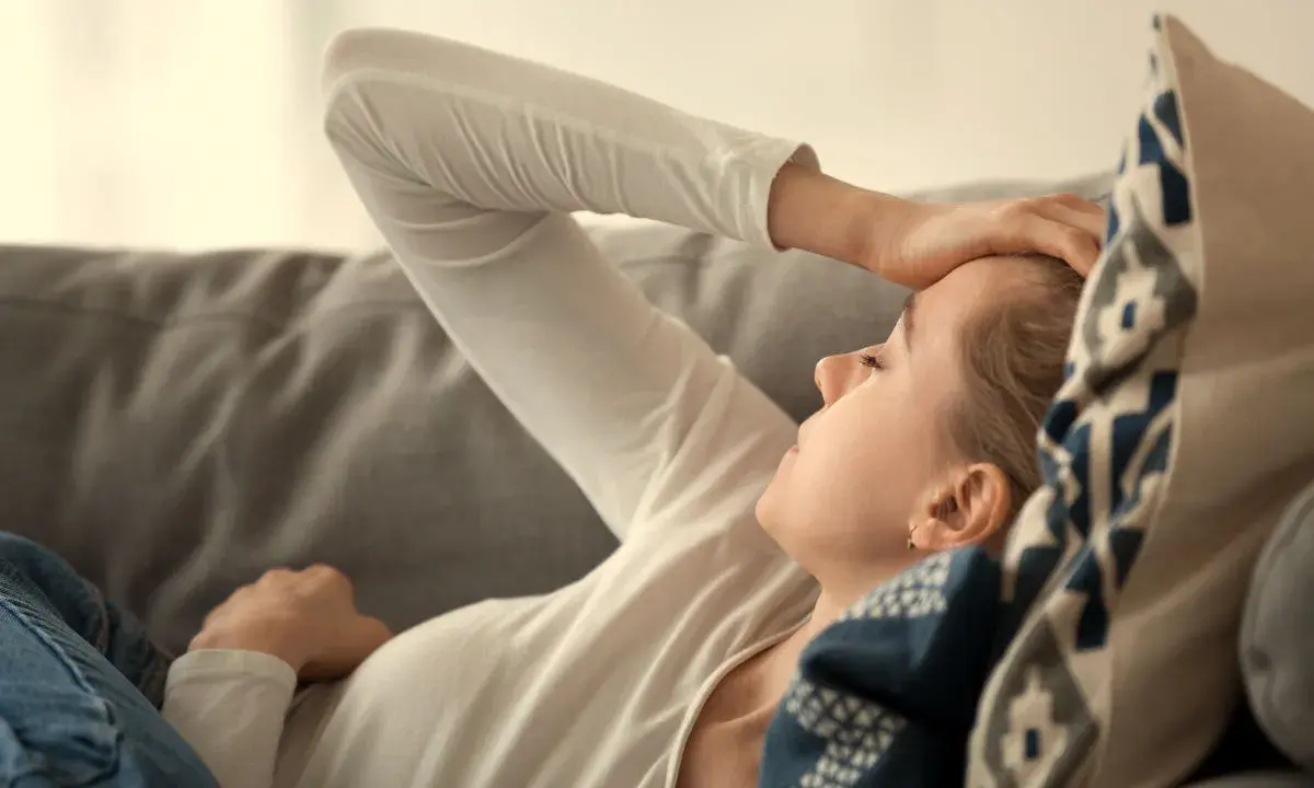 Kvinna med b2 brist ligger på en soffa med handen mot pannan, ser ut att ha ont.