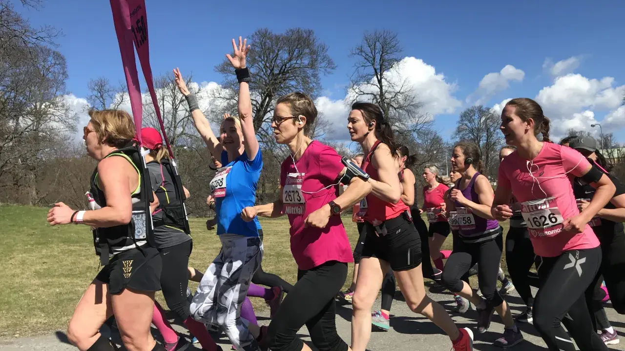 A group of women in running gear race on a sunny day, some with arms raised.