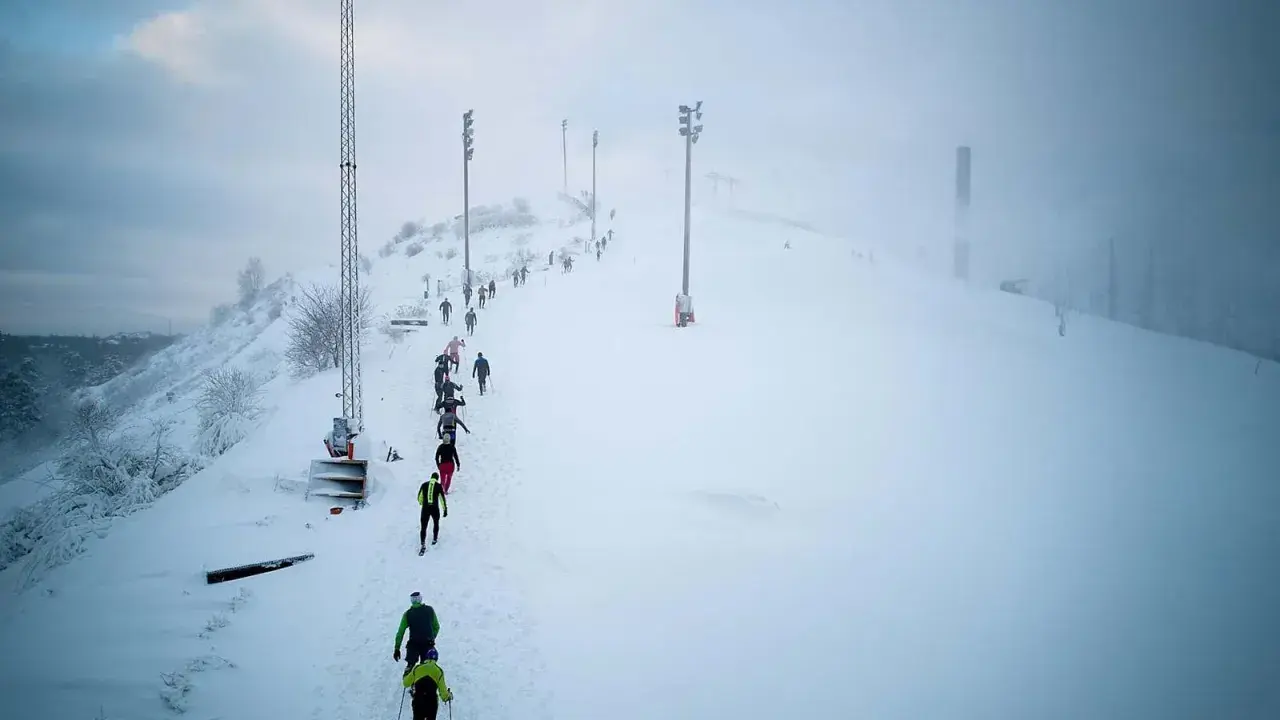 Deltagare i Hammarby Alpin Marathon kämpar sig uppför en snöig backe med skidstavar.