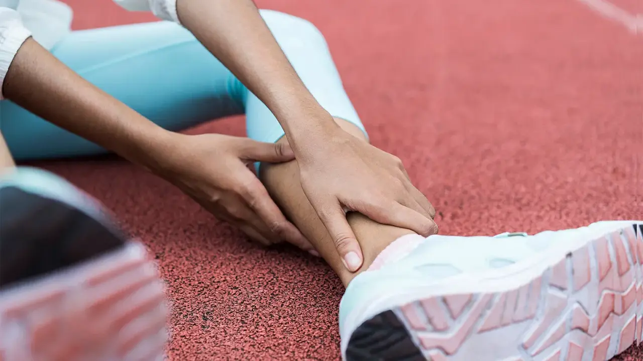 Person på löparbana med händer på underbenet, troligen för rehab benhinneinflammation.