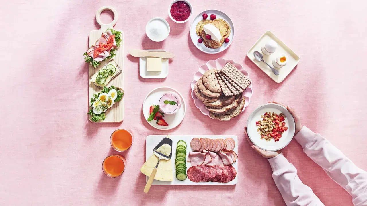 En härlig svensk frukost med smörgåsar, pannkakor, yoghurt, frukt, charkuterier och juice.