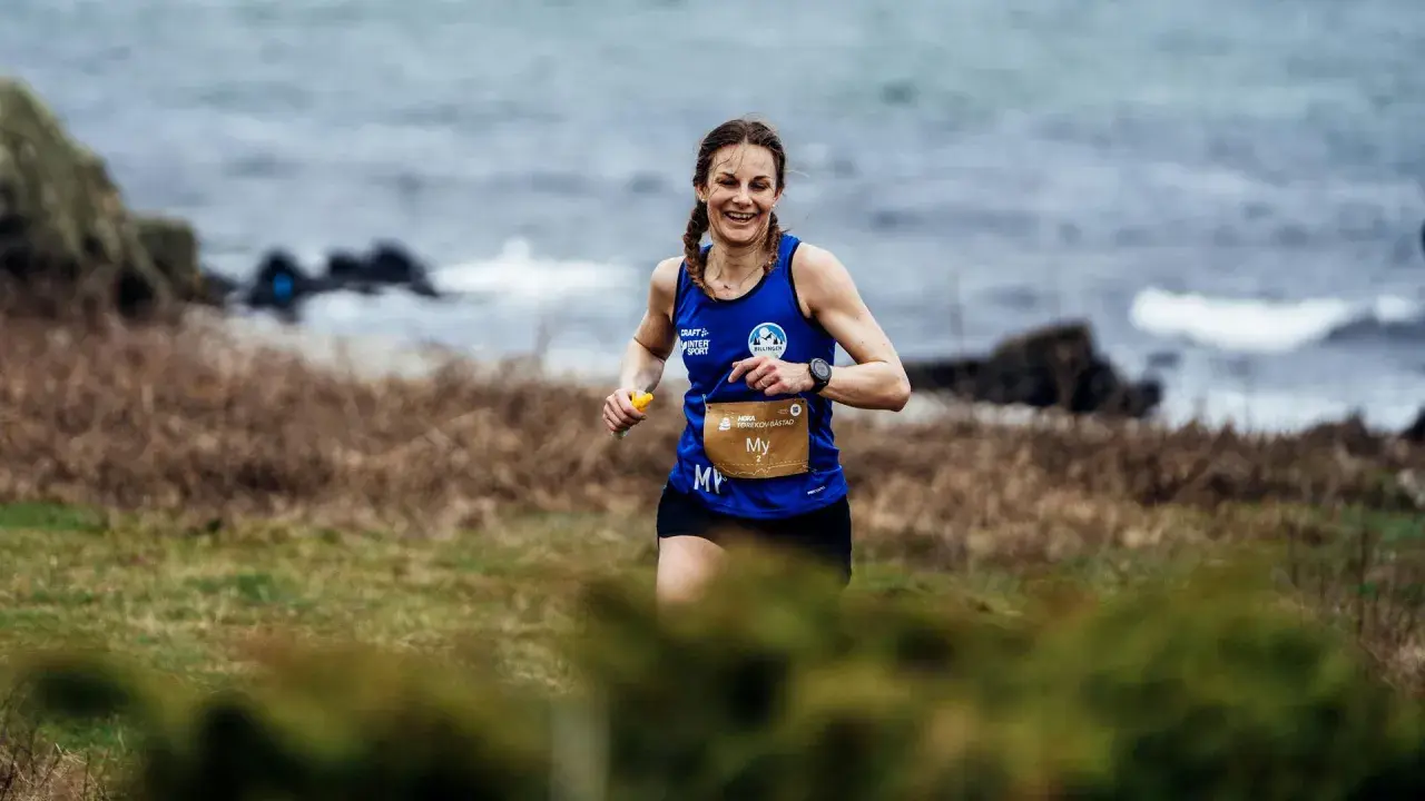 Woman running on a grassy trail by the sea, smiling.
