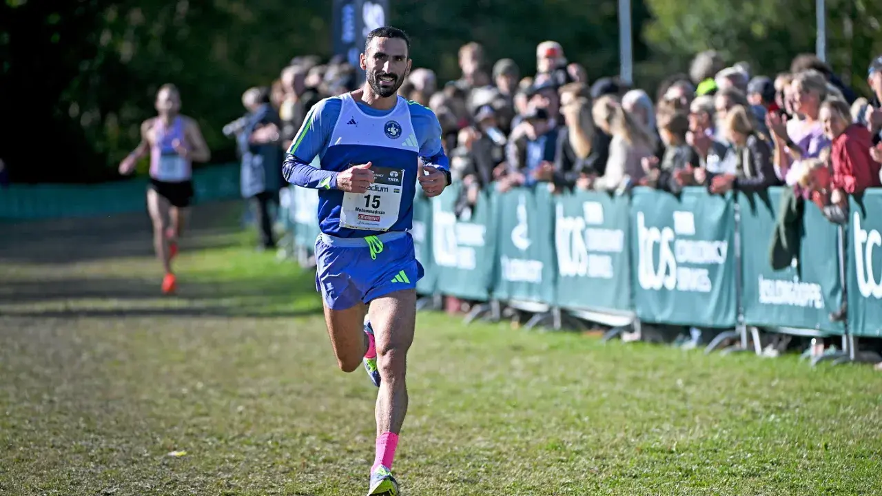 Löpare med nummer 15, klädd i blått och med rosa strumpor, springer mot publiken. En annan löpare syns i bakgrunden. Kanske är det en del av sevilla marathon.