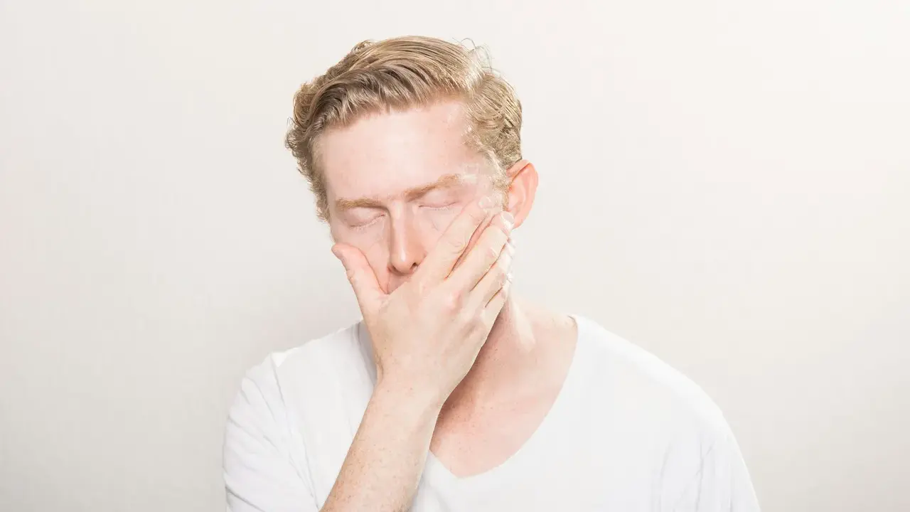 Man med slutna ögon och hand över munnen, som om han drabbats av en plötslig kramp i tårna brist.