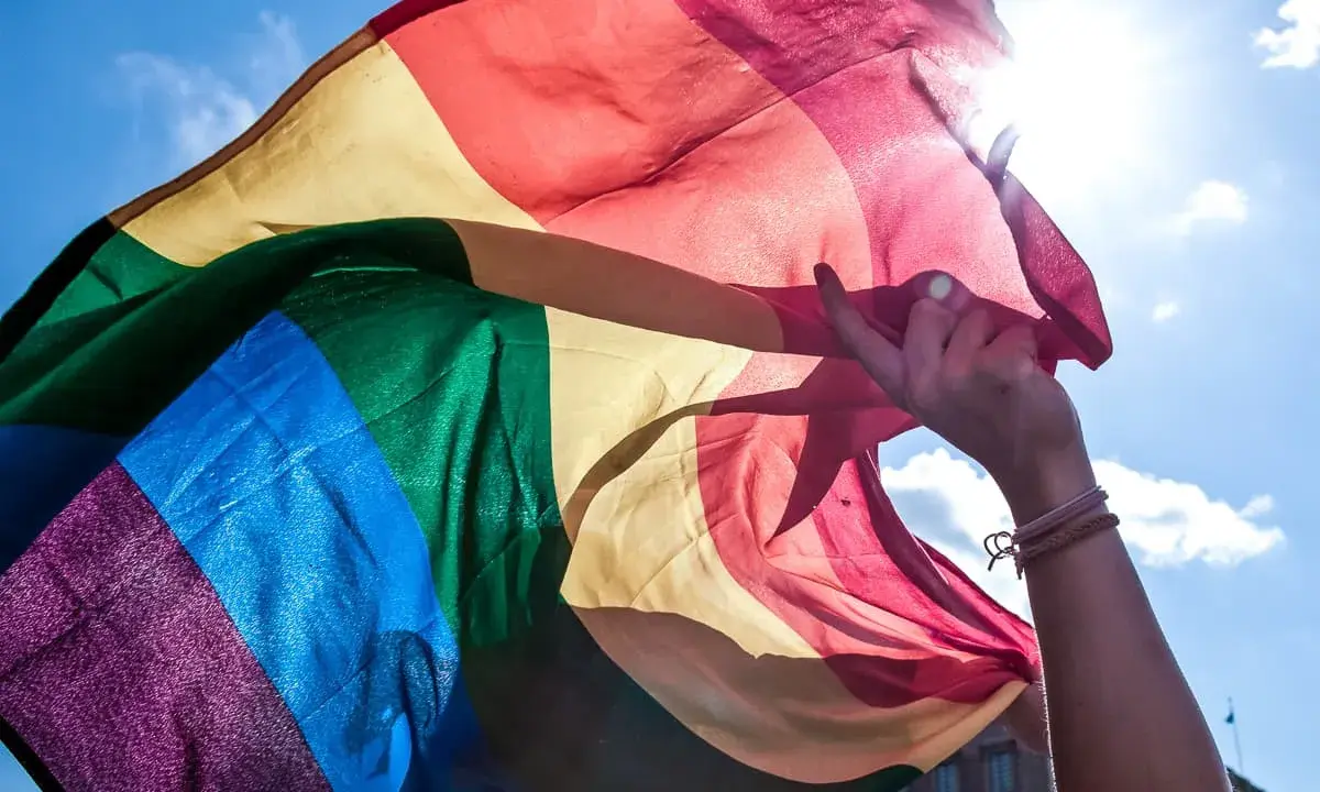 En hand håller en regnbågsflagga mot en solig himmel. En symbol för att **run for pride** och kärlek.