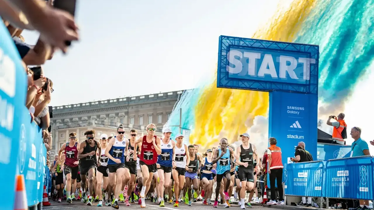 Löpare startar adidas halvmarathon i Stockholm. Publiken hejar och färgexplosioner lyser upp himlen.