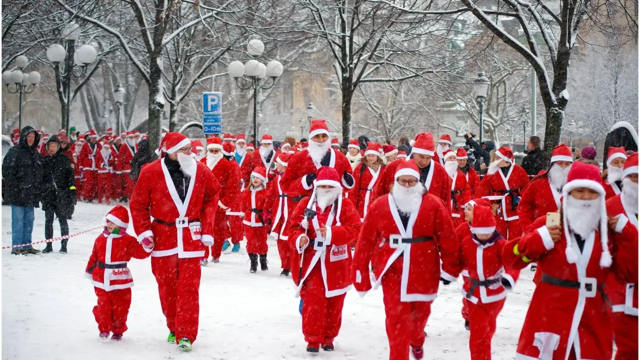 En stor grupp tomtar, både vuxna och barn, deltar i en snöig santa run.