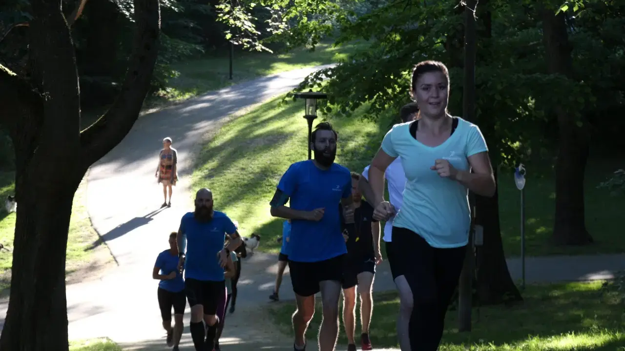 En grupp löpare i en park, en kvinna i ljusblå tröja springer framåt. Kanske undrar du vad betyder anaerob träning när du ser dem kämpa uppför backen.