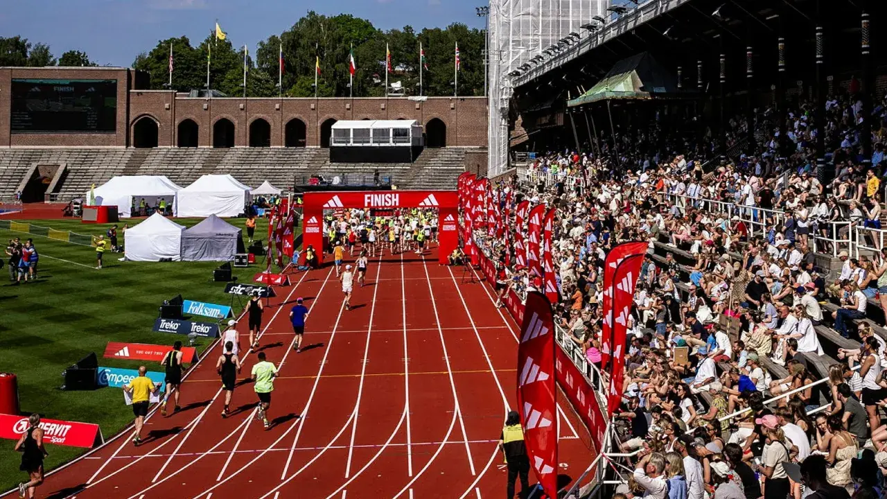 Löpare korsar mållinjen på stockholm marathon bana. Publiken jublar från läktaren.