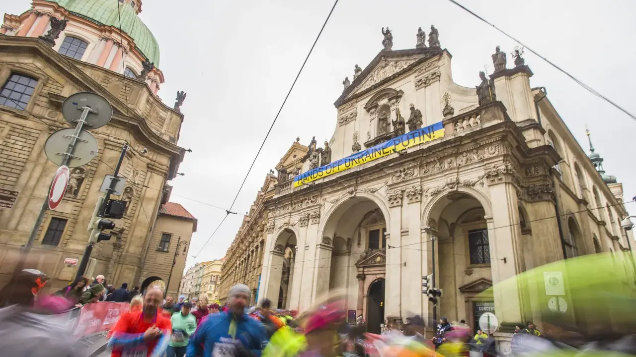 Löpare i Prag halvmarathon passerar en byggnad med en banderoll "HANDS OFF UKRAINE, PUTIN!".