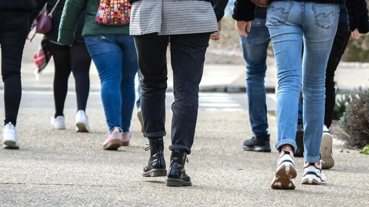En grupp människor går på en trottoar. De har på sig jeans och sneakers. Kanske är de på väg att nå sina 10000 steg kcal.