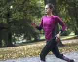 Kvinna springer i parken, fokuserad på att förbättra sin löpning. Frågan "hur blir man snabbare" besvaras med träning.