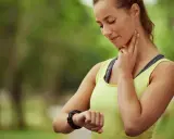 En kvinna kollar sin puls på halsen och handleden, nöjd med sin bra vilopuls efter träningen.