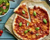 En härlig, nyttig pizza med tomatsås och ost, toppad med färsk basilika. Bredvid en fräsch sallad med gröna bönor och tomater.