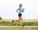 Kvinna i blå tröja och svarta shorts springer på en landsväg. Hon har en imponerande **run streak** och njuter av löprundan i det öppna landskapet.