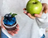 En hand håller ett grönt äpple, den andra en dekorerad cupcake. Ett val för en socker detox.