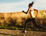 Kvinna i gult linne och svarta tights springer snabbt på en grusväg, en del av ett intensivt hiit pass.