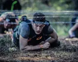En deltagare i ett ocr sport-lopp kryper under taggtråd.