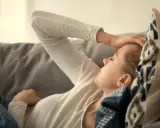 Kvinna med b2 brist ligger på en soffa med handen mot pannan, ser ut att ha ont.