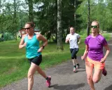 Tre kvinnor springer på en grusväg i en skogsmiljö, zon 2.