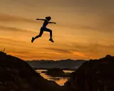 Silhuett av en kvinna som hoppar över en flod vid solnedgången, övervinner negativa tankar.