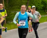 Glada löpare i ett 10 km lopp. En kvinna med nummer 8429 ler och gör segertecken.