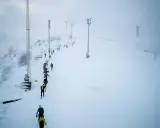 Deltagare i Hammarby Alpin Marathon kämpar sig uppför en snöig backe med skidstavar.