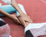 Person på löparbana med händer på underbenet, troligen för rehab benhinneinflammation.
