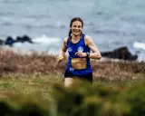 Woman running on a grassy trail by the sea, smiling.