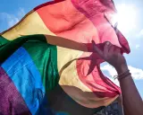 En hand håller en regnbågsflagga mot en solig himmel. En symbol för att **run for pride** och kärlek.