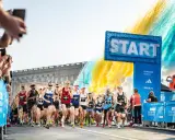 Löpare startar adidas halvmarathon i Stockholm. Publiken hejar och färgexplosioner lyser upp himlen.
