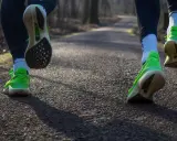 Två löpare springer långsamt på en grusväg i en skog. Deras neonfärgade skor syns tydligt.