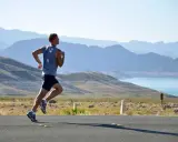 Man springer maraton längs en väg med berg och en sjö i bakgrunden.