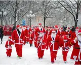 En stor grupp tomtar, både vuxna och barn, deltar i en snöig santa run.