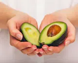 Händerna håller en avokado, delad på mitten, som visar dess gröna kött och bruna kärna. En näringsrik källa till avokado vitaminer.