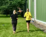 Två kvinnor njuter av en löprunda barfota på gräset en solig dag.