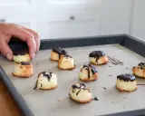 En hand lägger nyttiga kokostoppar med choklad på en plåt.