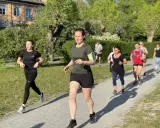 En grupp löpare på en grusväg, kanske på väg att klara 1 mil. Solen skiner och träden är gröna.