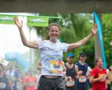 Glad kvinna med armarna uppe vid målgången i ett maraton. En lycklig löpare som njuter av sin maraton tid.