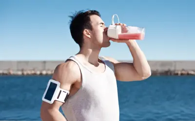 Man dricker rosa vätska ur flaska, kanske en proteinvatten bluff? Träningsarmband på armen.