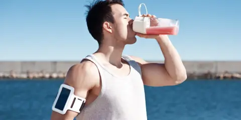 Man dricker rosa vätska ur flaska, kanske en proteinvatten bluff? Träningsarmband på armen.