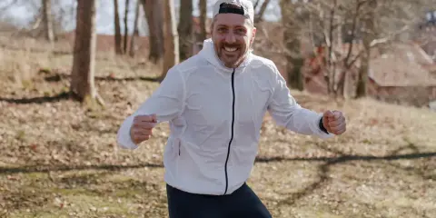 Glad löpare i vit jacka och keps, redo att springa. Undrar hur lång tid det tar att springa 1 mil?