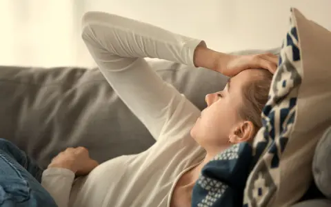 Kvinna med b2 brist ligger på en soffa med handen mot pannan, ser ut att ha ont.