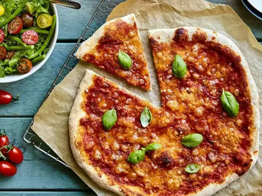 En härlig, nyttig pizza med tomatsås och ost, toppad med färsk basilika. Bredvid en fräsch sallad med gröna bönor och tomater.