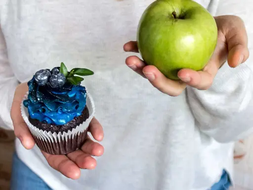 En hand håller ett grönt äpple, den andra en dekorerad cupcake. Ett val för en socker detox.