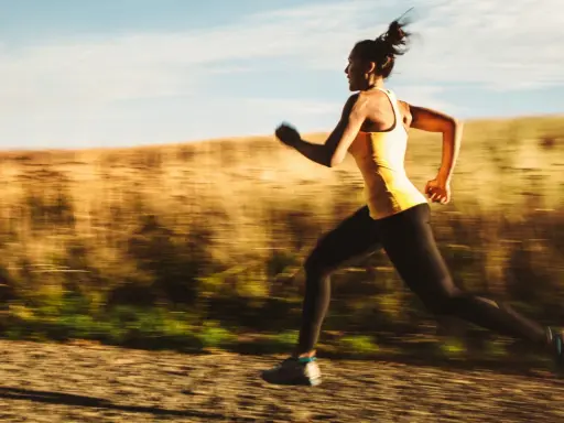Kvinna i gult linne och svarta tights springer snabbt på en grusväg, en del av ett intensivt hiit pass.